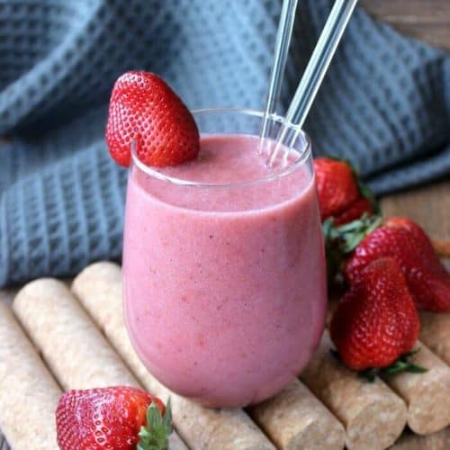 Bright pink smoothie poured in a glass with glass straws and a strawberry on the rim as garnish.