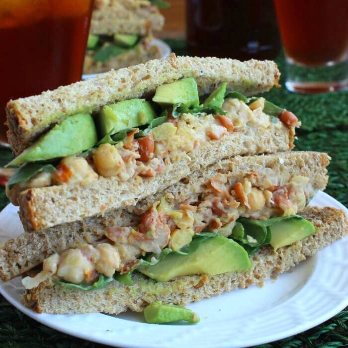 Loaded Chickpea Salad Sandwich is sliced in half and the halves are stacked on top of each other so you can see all of the colorful ingredients.