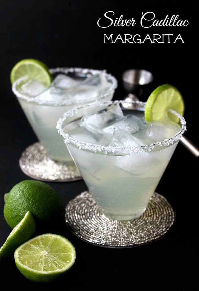 Silver Cadillac Margarita is silvery in hue and two flared glasses are filled over ice cubes. Lime slices are slid onto the salt covered rims.