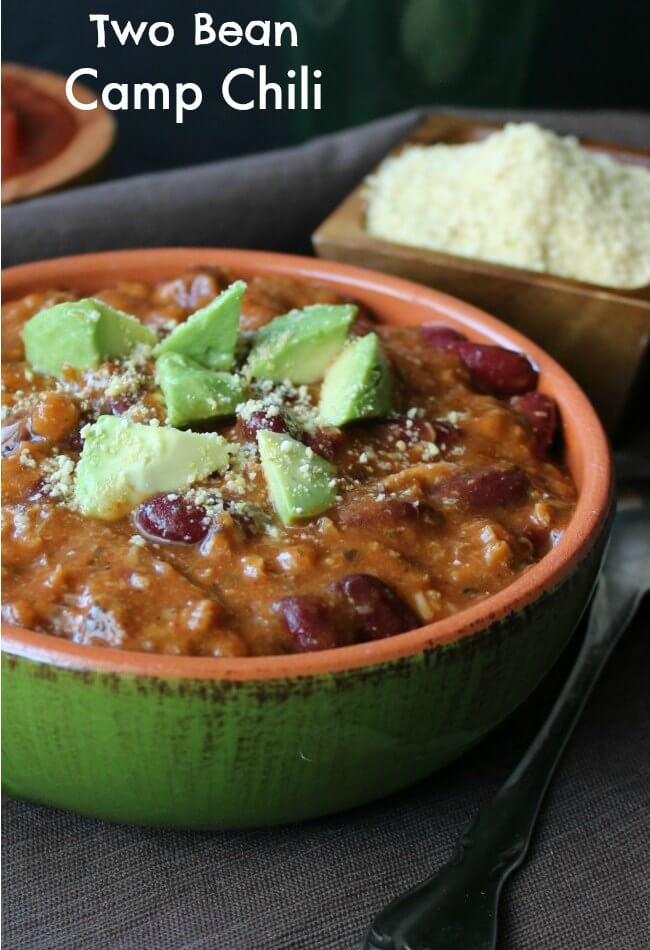 Two Bean Camp Chili is in a green pottery bowl that has two handles. It's piled high and sprinkled with avocado chunks and parmesan cheese.