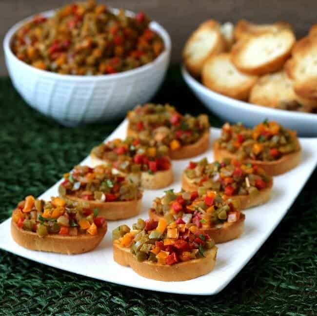 A tilted rectangle platte has loaded crostini lined up wit more bell pepper bruschetta crostini.