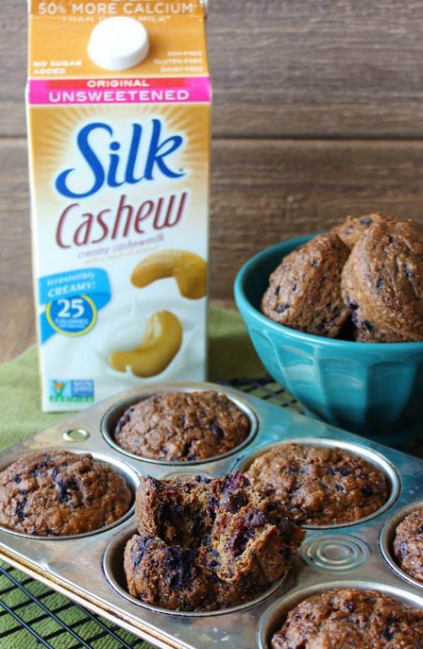 Black Forest Cherry Muffins broken open in a muffin tun and sitting in front of a carton of Silk cashewmilk.