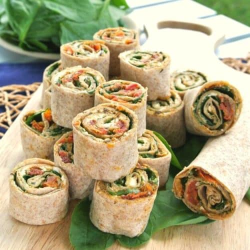 Sun-Dried Tomato Pesto Tortilla Rollups are sliced and stacked on a wooden cutting board and placed on the picnic table for everyone to enjoy.