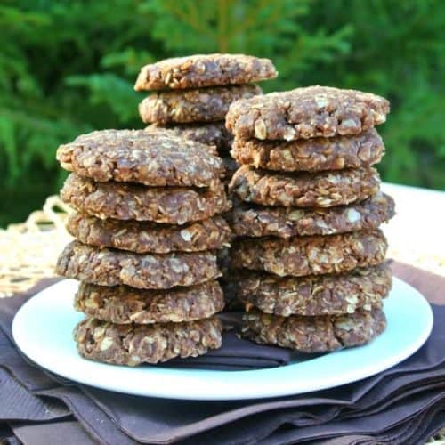 No Bake Chocolate Peanut Butter Cookies are stacked in three piles of overlapping stacks with about 7 cookies to the stack. All on a white plate on top of brown napkins.