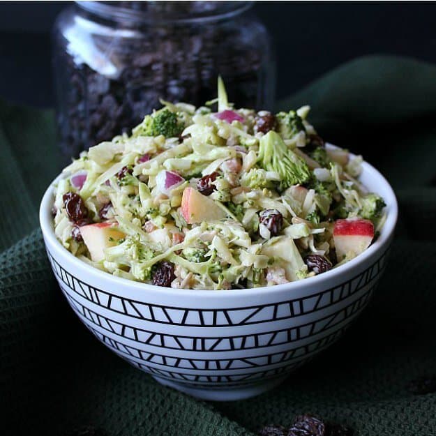 Vegan Apple Broccoli Salad is vividly colored in a zigzag patterned black and white bowl. Finely chopped vegetables and fruit fill the bowl. All against a black backdrop.