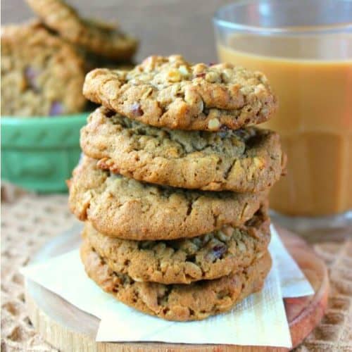 Dairy-Free Oatmeal Cranberry Cookies stacked 5 high on two golden napkins with an iced coffee on the side with a bowl of more cookies.