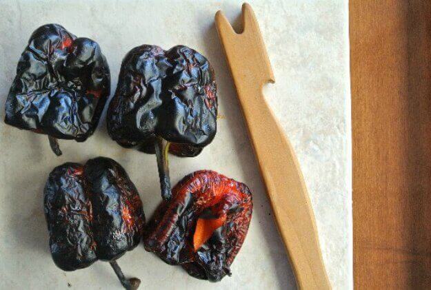 Blackened Roasted Red Bell peppers ready for stripping laying next to a wooden tool made for me as protection when pulling pans out of the hot oven.