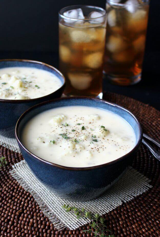 Healthy cauliflower soup with two bowls sitting in front of two glasses of iced eat.