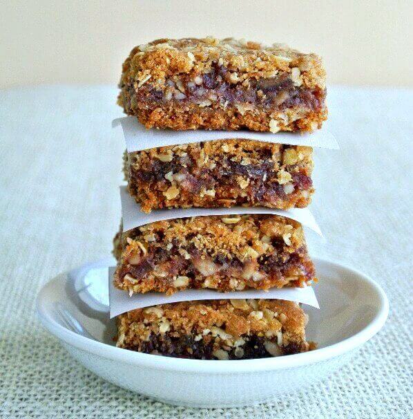 A stack of layered square treats are stacked four high with a parchment square separating each.