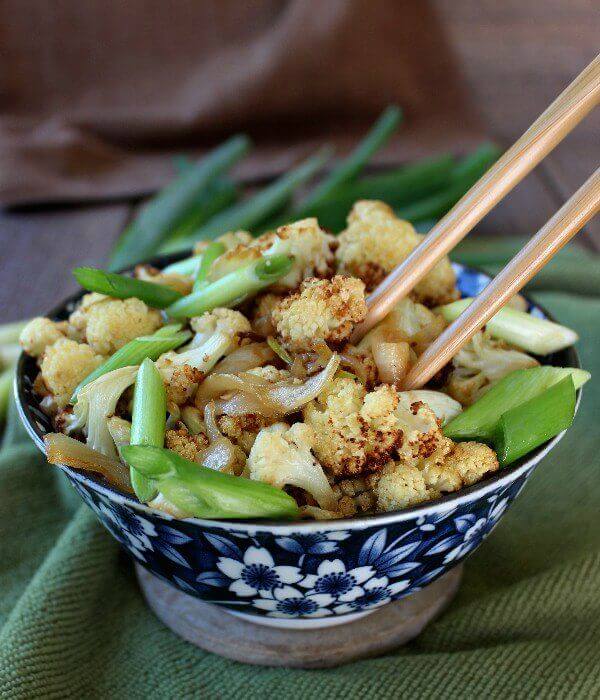 An Asian styled blue and white bowl holding cooked cauliflower with scallions and chopsticks inside of bowl too.