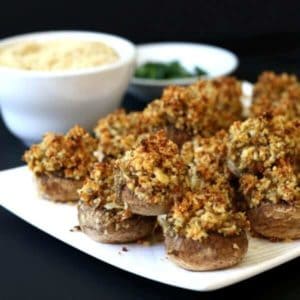 Easy Stuffed Mushrooms are layed out in rows on a white triangle plate wiuth dipping sauce next to them.