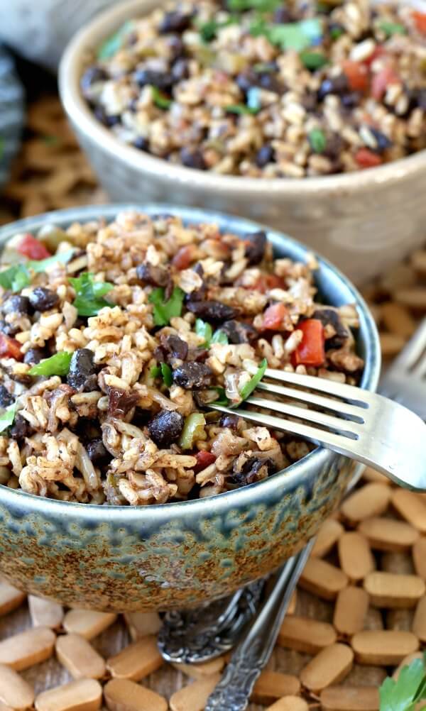 Acadian Black Beans and Rice up-close view of the recipe for a better look of a perfect side dish. A fork is balancing on the full bowl of colorful contrasting black beans and brown rice.