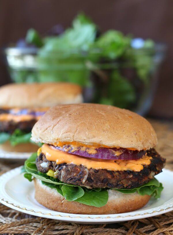 Black Bean Burgers Recipe with two plates of ready-to-eat bean burgers and fresh salad set behind.