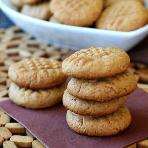 Maple Peanut Butter Cookies are shown in two stacks of cookies on a brown napkin with more in a bowl behind.