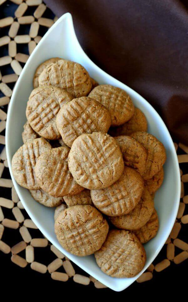 Maple Peanut Butter Cookie are stacked in a white swirl bowl that has pointed tips on each end. All is sitting on an open worked mat.