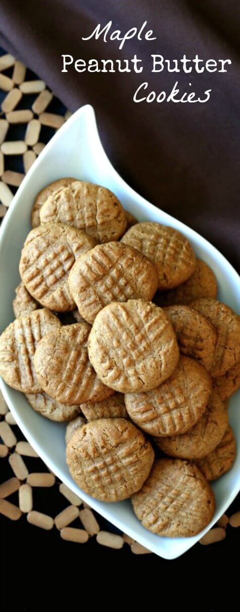 Maple Peanut Butter Cookies are stacked high in a swirled white bowl. An overhead shot with them sitting on a open weave mat and a chocolate cloth napkin.
