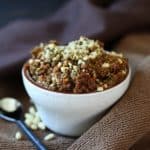  Vegan Sun Dried Tomato Pesto in a small specked beige bowl with pine nuts sprinkled around.