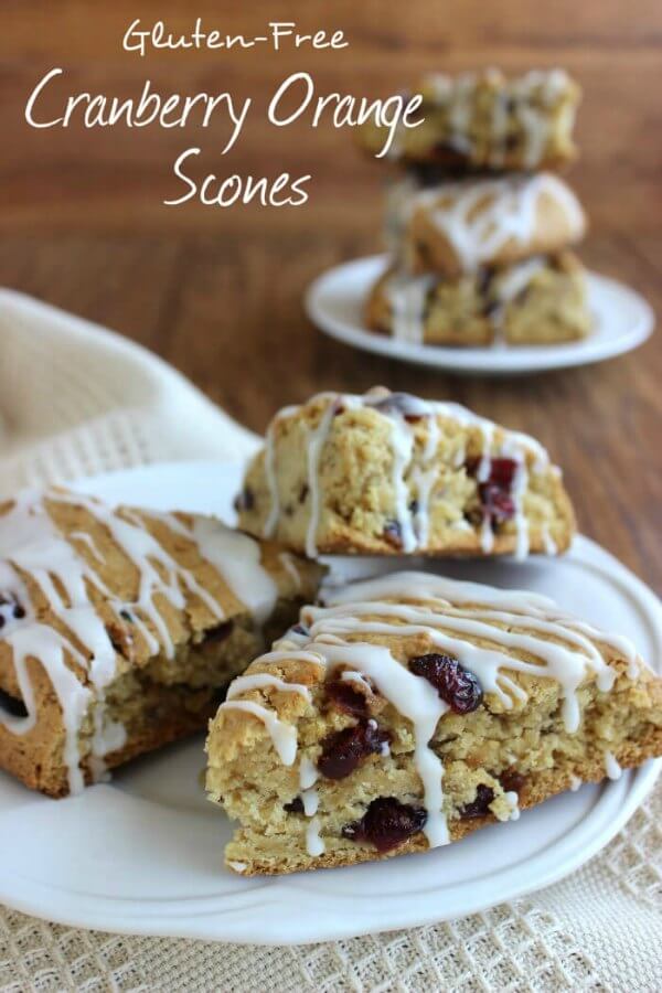 Three iced scones on a white plate with a stack behind and all are on a wooden table.
