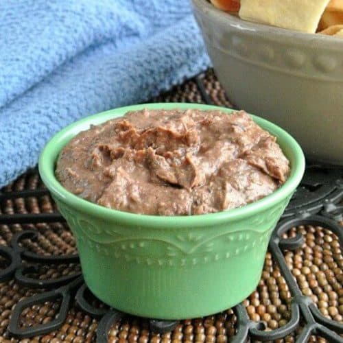 Black bean dip is to the top of a small green bowl with chips on the side for dipping.