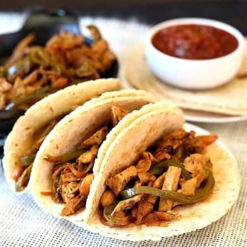 Vegan Fajitas with Meatless Chicken are sitting three to a plate with salsa on the side.