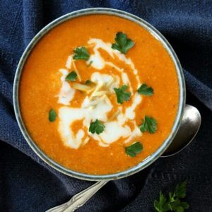 Cauliflower Tikka Masala Soup is bright orange with swirls of thick vegan cream and parsley garnish.