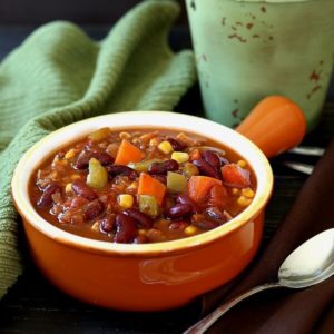 Veggie chili is filling a terra cotta handled chili bowl with carrots, beans and more showing clearly.