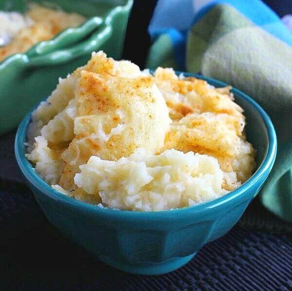 Mashed Potato Casserole is scooped up in a turquoise bowl and tilted forward.