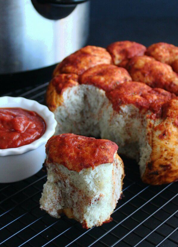 A tall fat loaf of pull apart bread with pizza sauce topping and throughout.