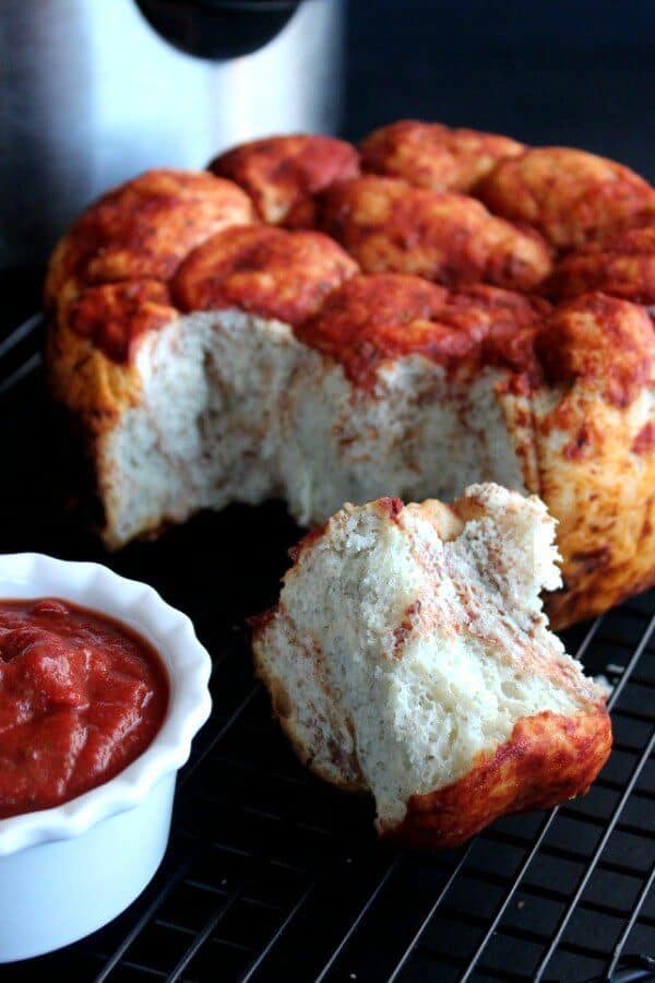 A tall fat loaf of pull apart bread with pizza sauce topping and throughout.