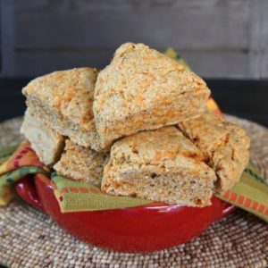 Chipotle Scones are speckled with orange dairy free cheese and red chipotle bits. Twelve triangle scones piled high in a red handles pottery bowl.
