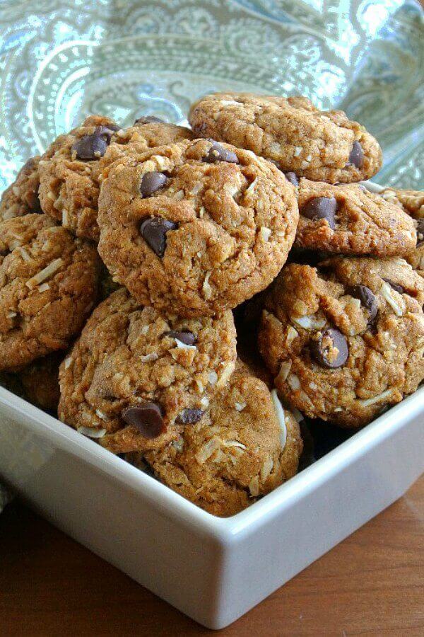 Coconut Chocolate Chip Cookies stacked to overflowing in a square ivory colored bowl.