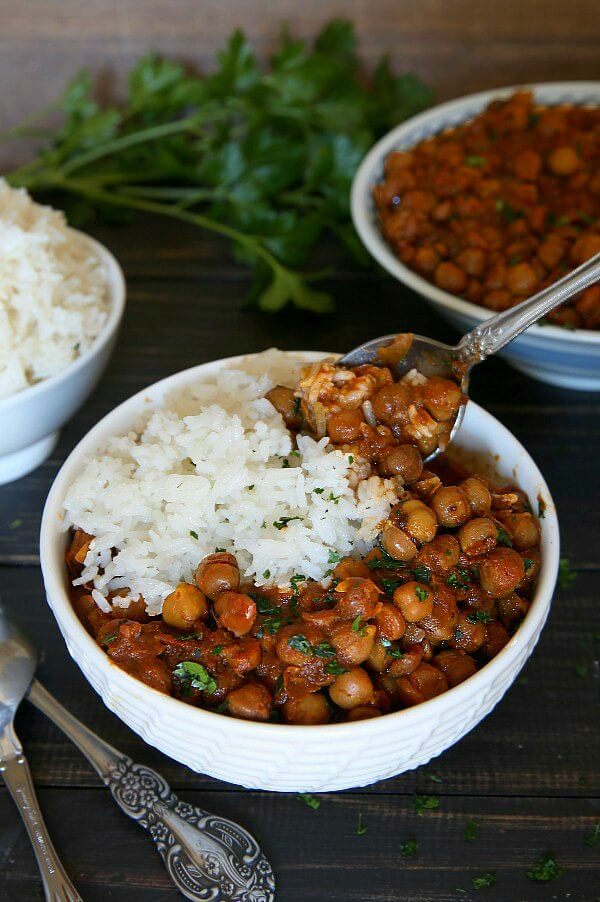 Rich red curry and chickpeas in a white bowl along side rice and a big spoonful coming your way.