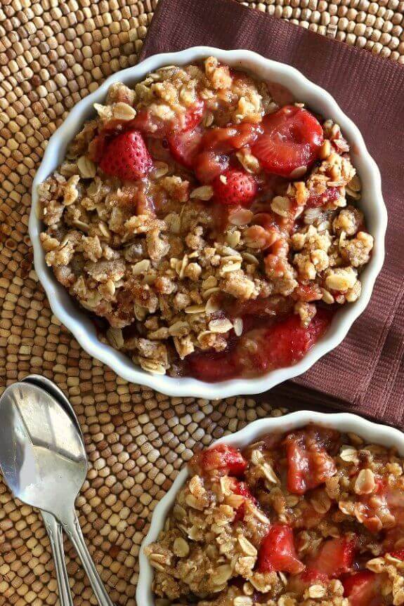 Slow Cooker Strawberry Crisp is filling a scalloped white bowl. A view from above with sweet sliced strawberries with an oat like strudel.