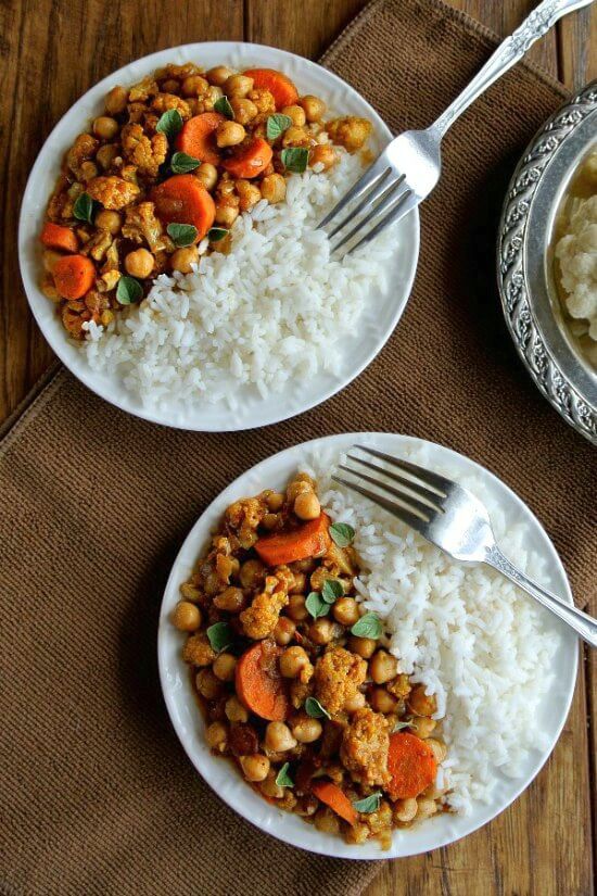 Overhead view looking down at two white plates. Each is split in half with Jasmine rice and cauliflower and carrots curry.