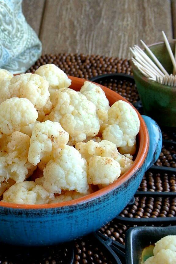 Mildly Marinated Cauliflower in off-center in a blue handled bowl filled with bite sized florets and lightly sprinkled with golden shades of coconut sugar pickling marinade.