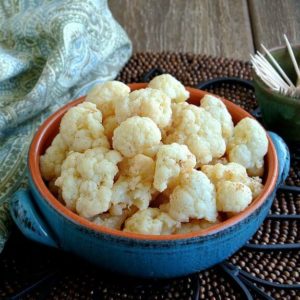 Mildly Marinated Cauliflower is speckled with spices and has a close-up view in a blue handled bowl on an iron trivet.