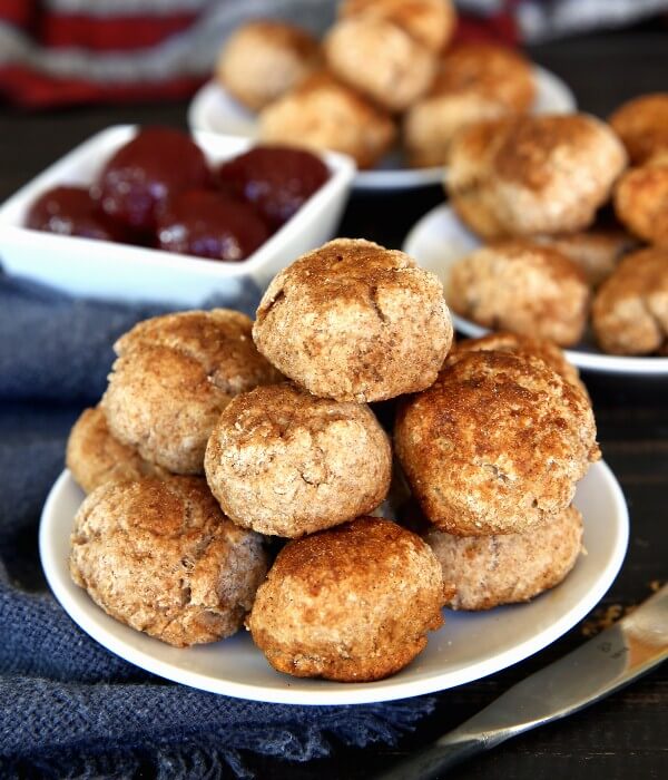 Cinnamon Cookie Biscuits are only about 2: wide and they are piled high on a white plate with stacks behind. Balls of strawberry jam are in a little bowl behind.