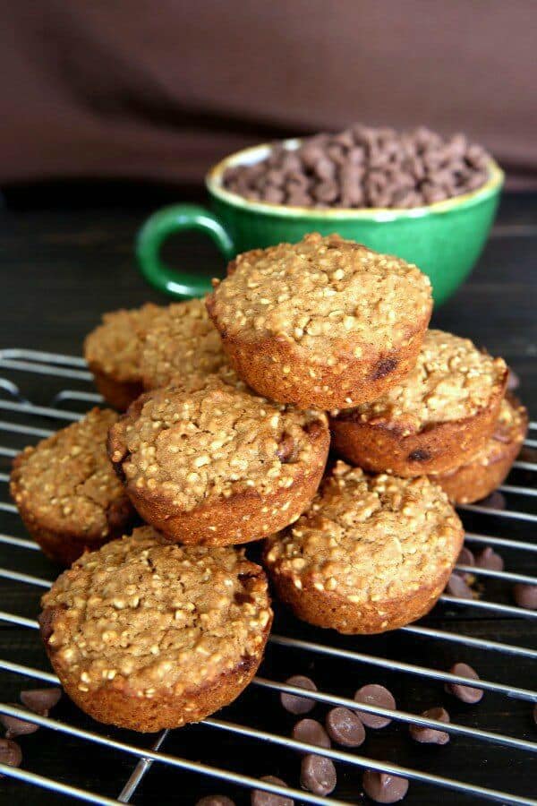 Irish Oatmeal Chocolate Chip Muffins are stacked high on their cooling rack with chocolate chips sprinkled around.