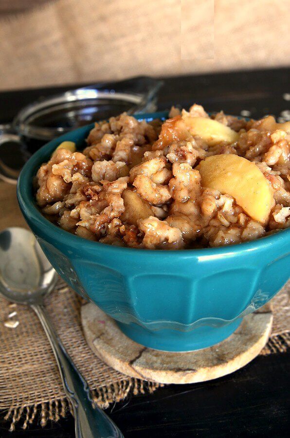 Slow Cooker Apple Oatmeal is heaped in a turquoise bowl with golden apples peeking out.