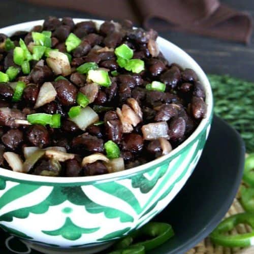 Slow Cooker Cuban Black Beans Recipe is piled high in a bright green and white bowl with a sprinkling of diced green jalapeño peppers.