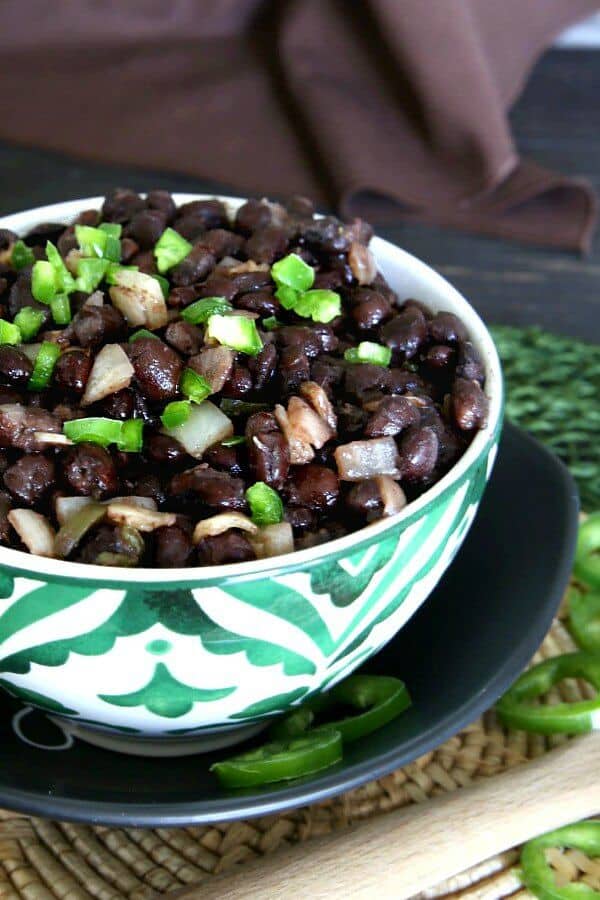 Slow Cooker Cuban Black Beans Recipe is piled high in a bright green and white bowl with a sprinkling of diced green jalapeño peppers.