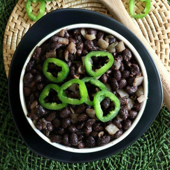 Slow Cooker Cuban Black Beans Recipe as an overhead shot with black beans in a white dish surrounded by black and green with jalapeño sliced rings on top.