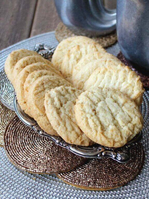 Almond Sugar Cookies are golden and are fanned out on a silver tray. Sitting in front of two pewter mugs.