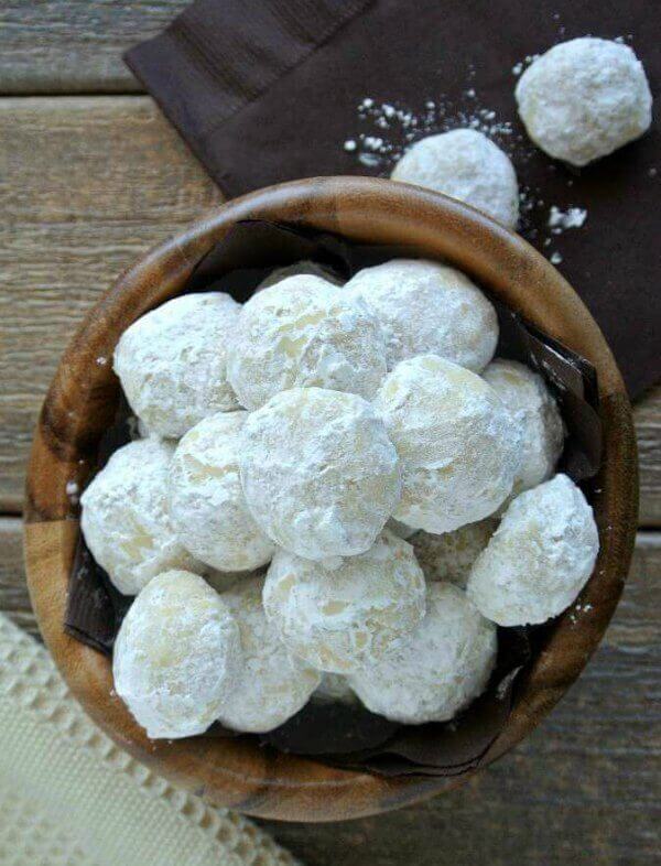 Mexican Wedding Cookies are covered with powdered sugar and being looked at from overhead. In a small dark wooden bowl.