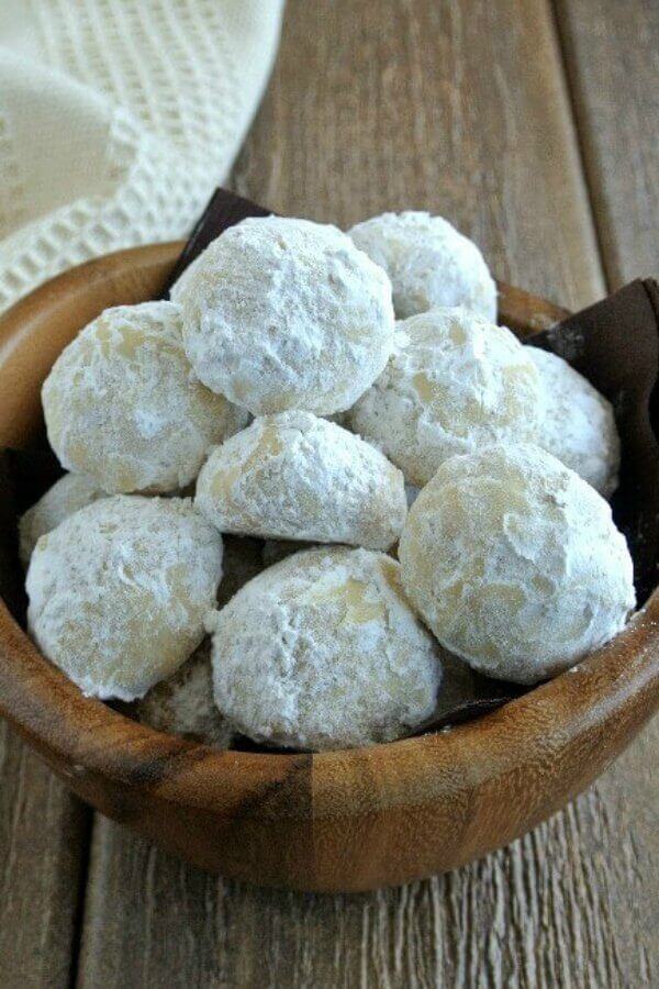 Mexican Wedding Cookies are covered with powdered sugar and are filling a small undulating wooden bowl.