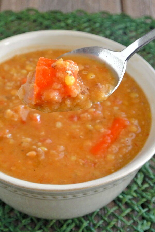 Slow Cooker Red Lentil Soup is o close-up of the rich orange soup in a white bowl. A spoon is holding a big bite up to you, front and center.