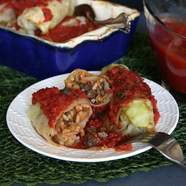 Vegan Cabbage Rolls Recipe is cabbage rolled around a flavorful mushrooms, rice and lentils. Two rolls are set on a white plate and opened to show the savory mixture inside.