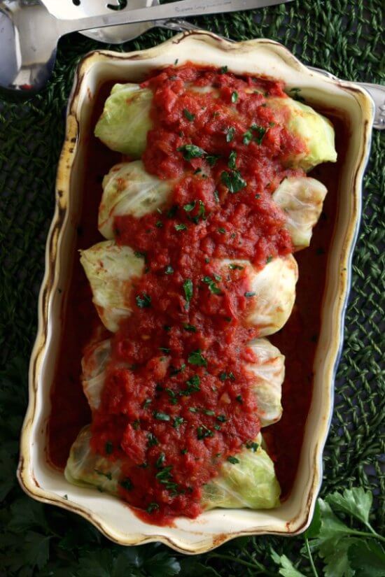 Vegan Cabbage Rolls Recipe is steamed cabbage rolled around a flavorful mushrooms, rice and lentils. Overhead photo of 5 rolls topped with a rich red sauce down the center.