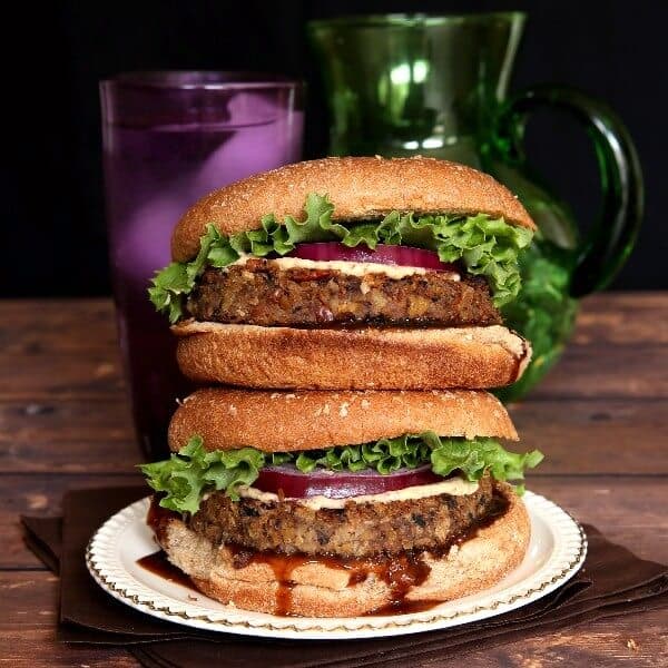 Vegan Mushroom Pecan Burgers are stacked double high with layers of curly lettuce, red onion and dripping hoison sauce.
