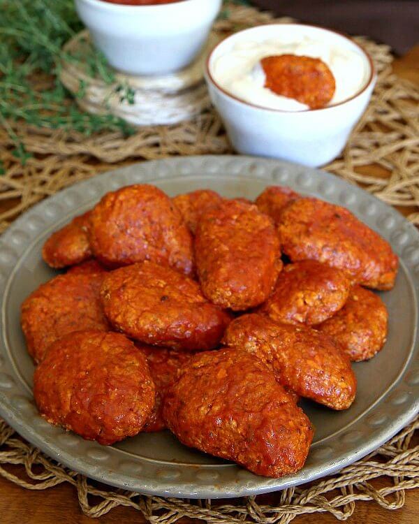 Boneless BBQ Buffalo Wings are angled forward on a rustic beige plate and shining in sparkly red sauce with a kick of heat.
